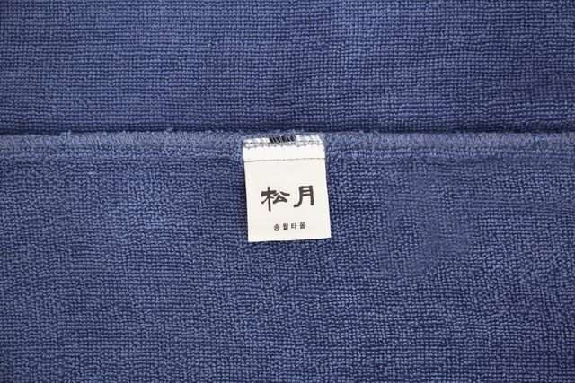 송월 30수라이트가운 30수라이트가운의 원단 표면과 송월 브랜드표를 가까이 보여 주는 모습